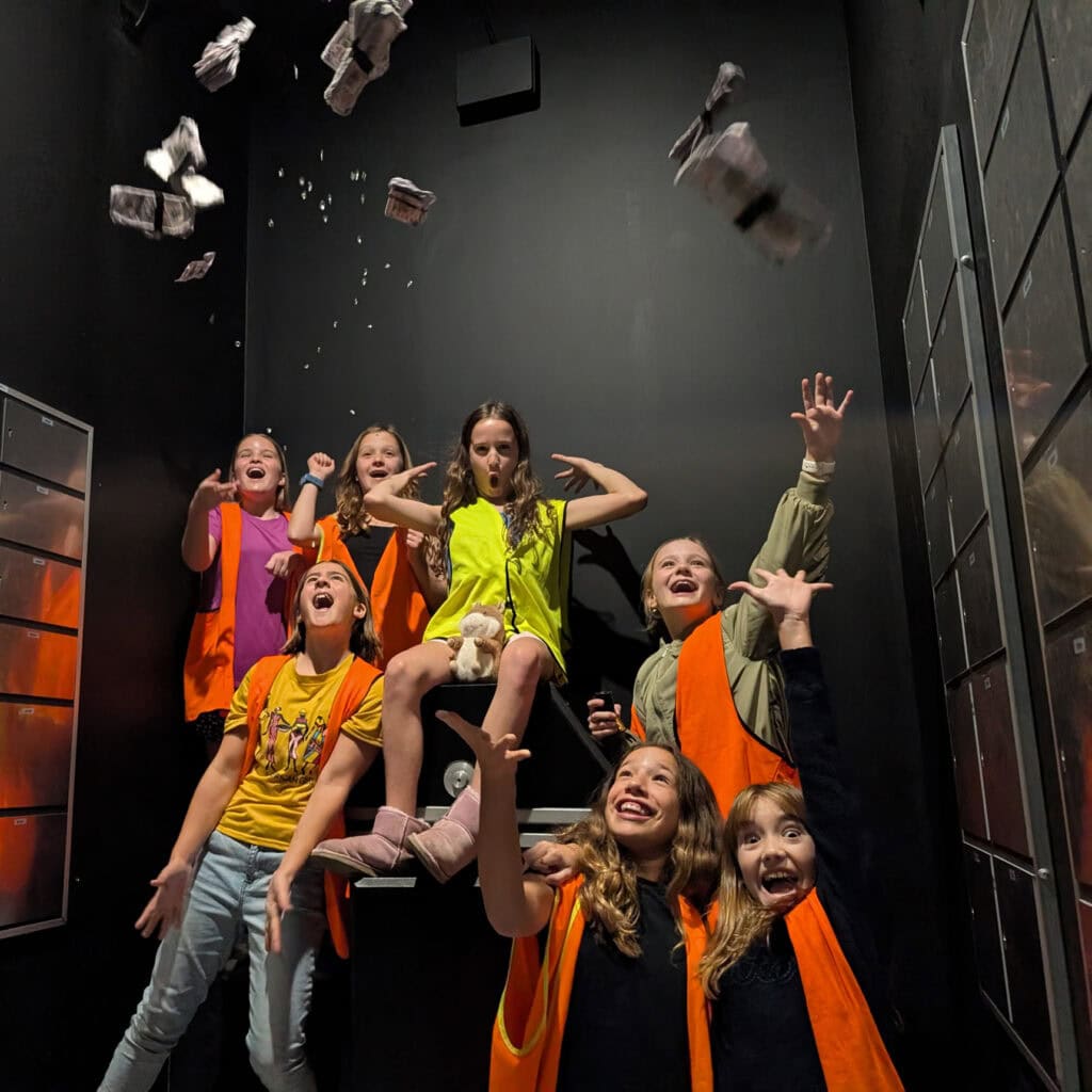 A group of children in a bank vault with their hands in the air.